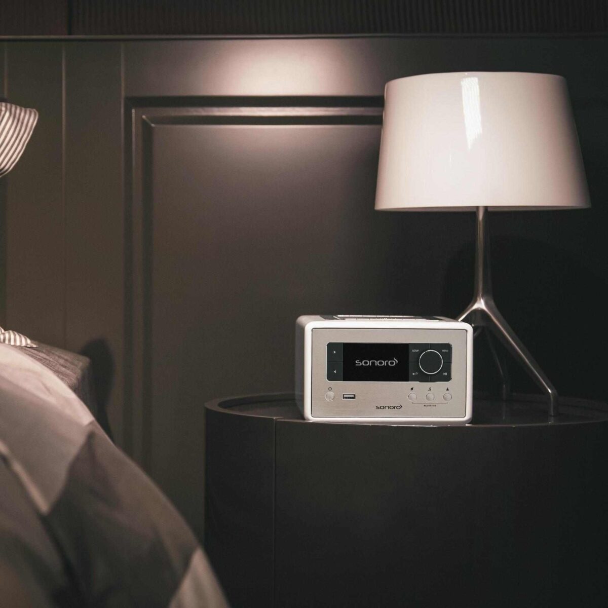 Sonoro RELAX Kompaktsystem in Weiß – stilvoll auf Nachttisch neben moderner Leuchte in gemütlicher Schlafzimmeratmosphäre.
