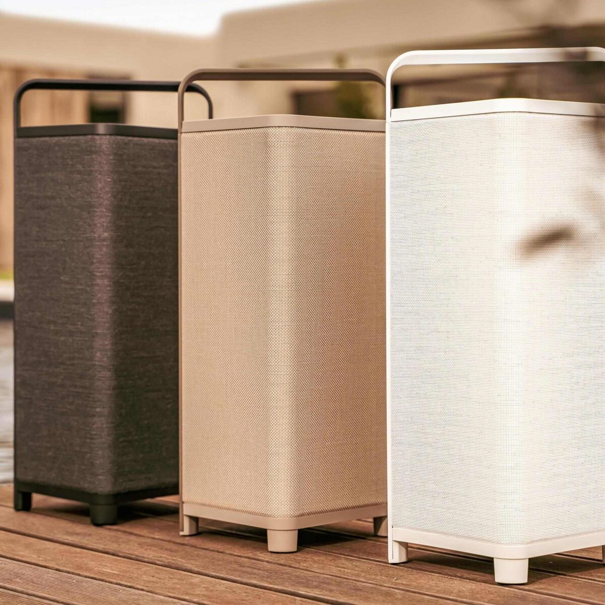 Drei ESCAPE P6 AIR Design-Lautsprecher nebeneinander – in Schwarz, Beige und Weiß – auf einer Terrasse mit stilvoller Outdoor-Kulisse.