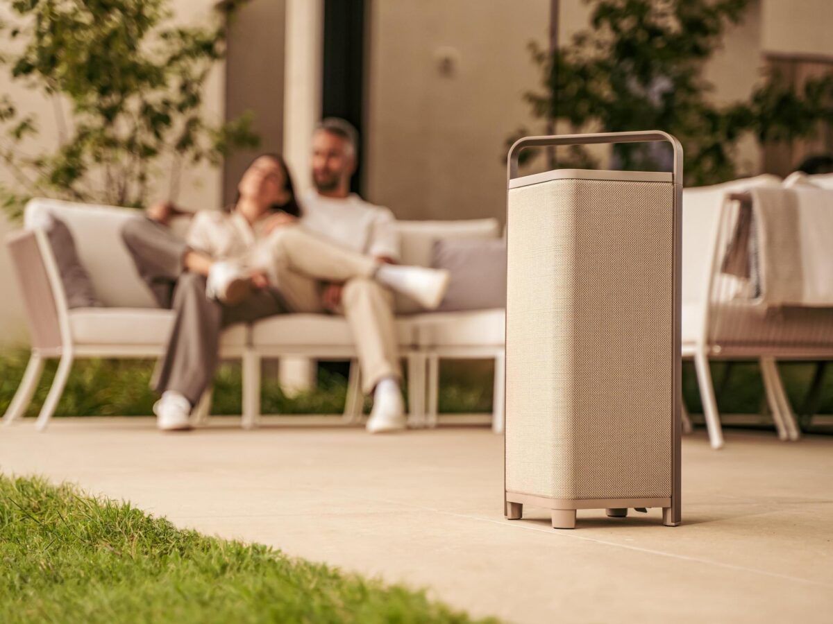 Zwei Personen entspannen auf einem Sofa im Garten, im Vordergrund steht ein Escape P6 Lautsprecher von sonoro in der Farbe Tan auf der Terrasse